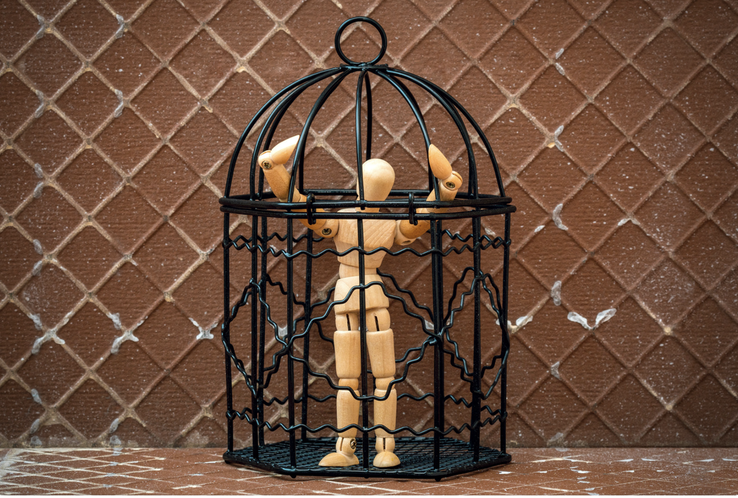 Wooden artist model locked in a black bird cage brown background